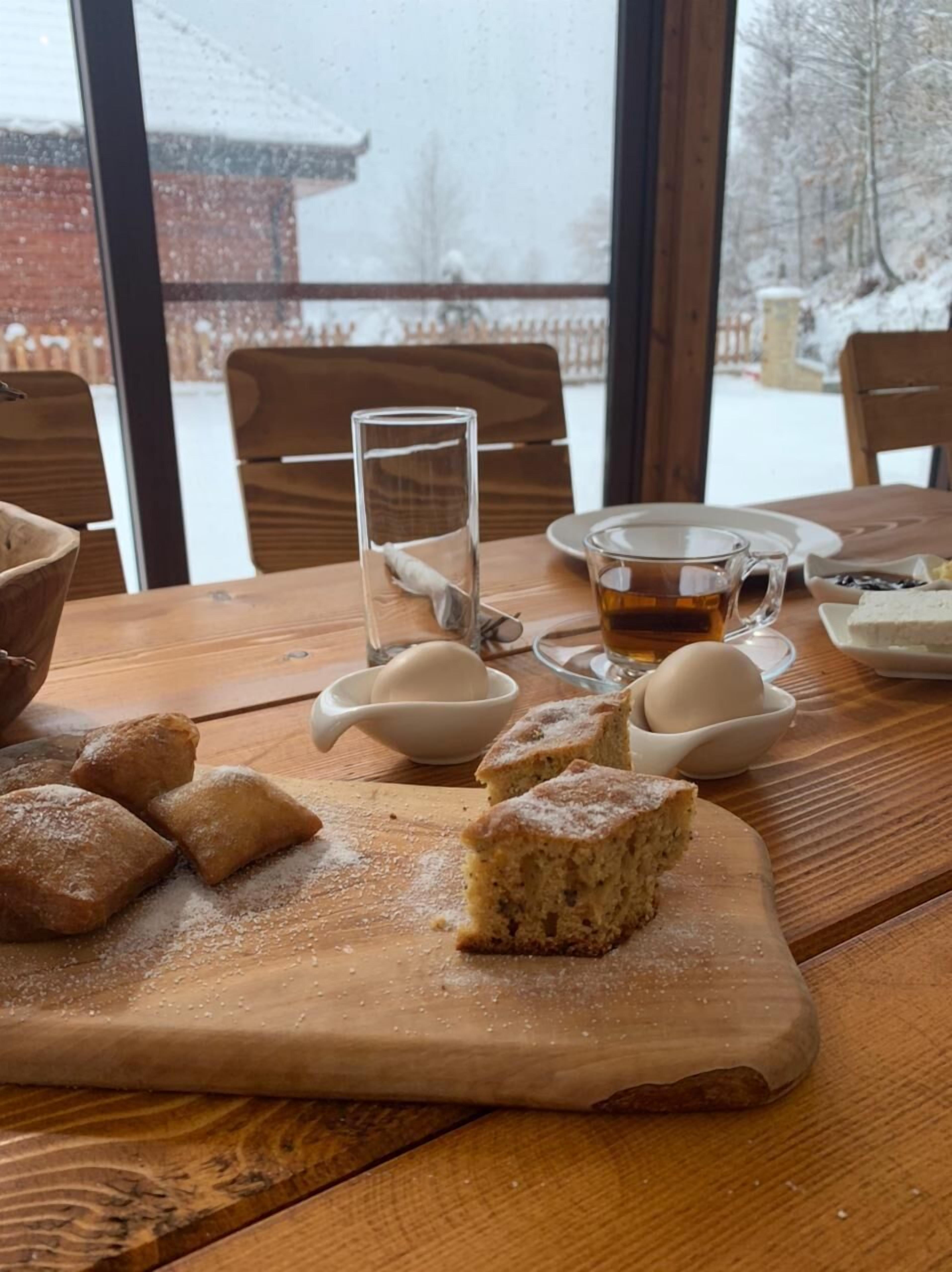 Una mesa de madera con una taza de té, pasteles y una copa de vidrio transparente.