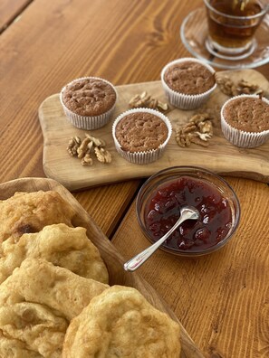 A wooden table with muffins in paper liners, a bowl of jam with a spoon, and a wooden tray with cookies.