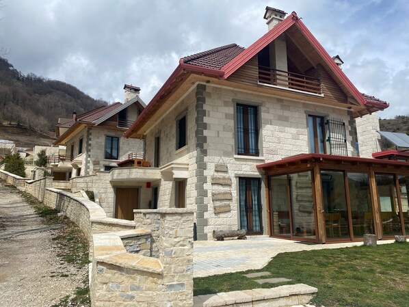 A stone house with a red roof, large windows, and a balcony.