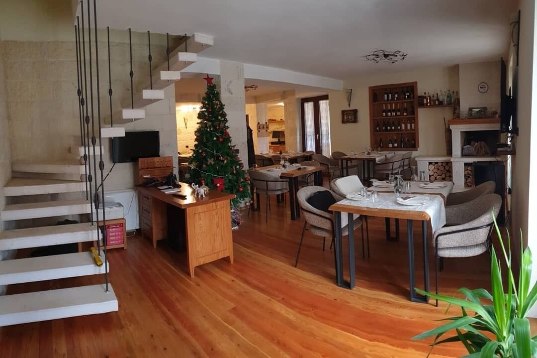 A spacious living area with a wooden staircase, a dining table set for four, a Christmas tree, and a fireplace.