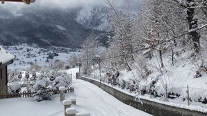 A snow-covered pathway leading to a building with a stone wall and a wooden roof.