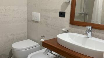 A bathroom with a toilet, bidet, sink, mirror, and a trash bin.