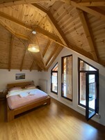 A bedroom with a wooden ceiling, a bed, and large windows.