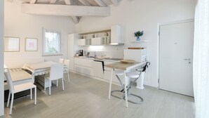 A modern kitchen with white cabinetry, a dining area with a table and chairs, and a window with sheer curtains.