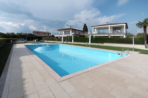 Una piscina con solárium empinado, rodeada por un césped cuidado y una casa moderna al fondo.
