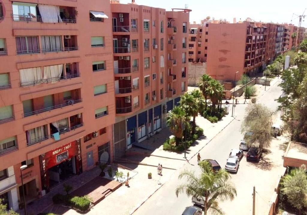 Um edifício residencial com várias andares, sacadas, uma rua na frente e carros estacionados.