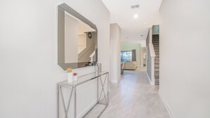 Ein moderner Flur mit einem Glastischchen, einem großen Spiegel und einer Treppe, die in einen anderen Raum führt.