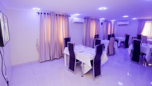 Un espace repas avec des tables et des chaises, des climatiseurs et des rideaux.