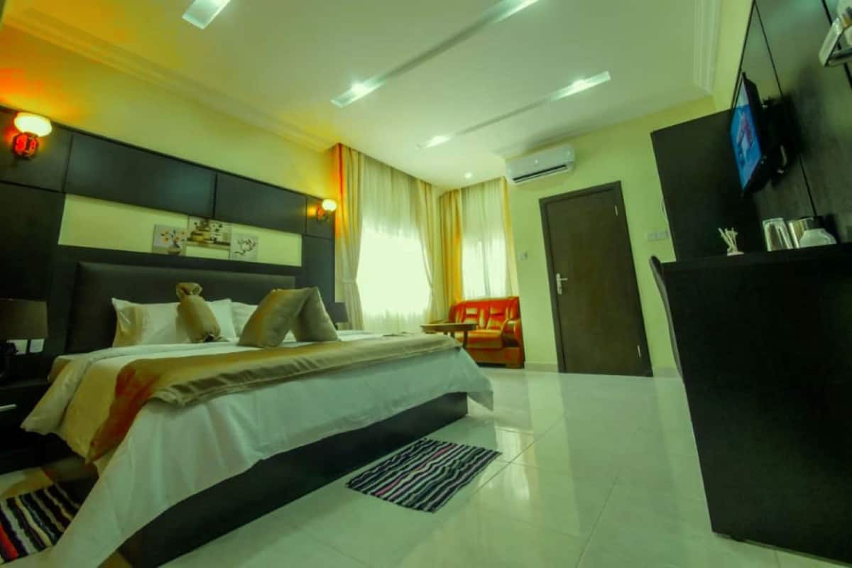 A hotel room with a bed, bedside table, lamp, air conditioning unit, TV, and a desk with a chair.