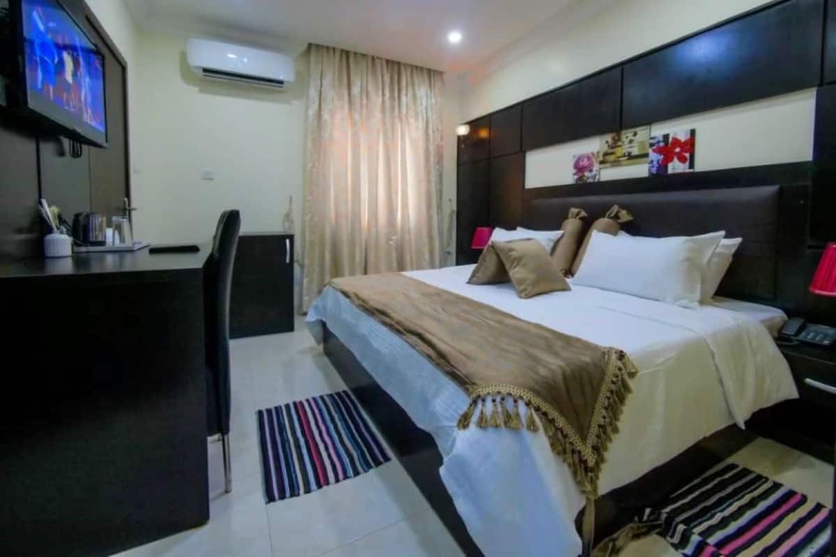 A hotel room with a bed, a desk, a chair, a television, and an air conditioning unit.