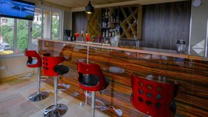 Un espace bar moderne avec un plafond en bois, des tabourets de bar rouges et un grand écran de télévision.