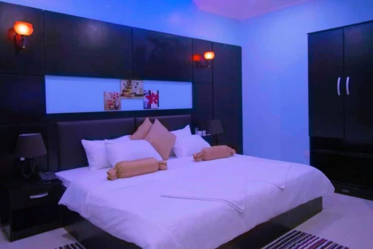 A modern bedroom with a large bed, dark cabinets, and ambient lighting.
