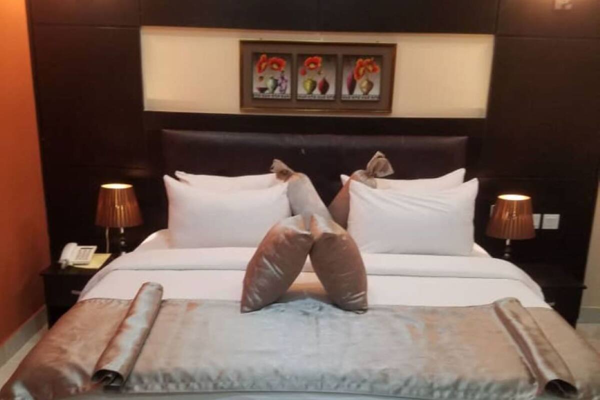 A hotel room with a large bed, two bedside lamps, a framed artwork above the bed, and a striped rug on the floor.