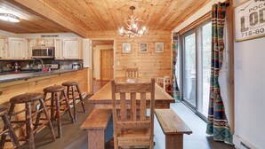 A wooden interior with a dining area, bar stools, a wooden table, and a kitchen with a microwave and cabinets.