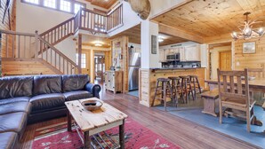 A spacious living area with a leather sofa, a wooden coffee table, and a red rug. A staircase leads to an upper level, and a kitchen is visible in the background.