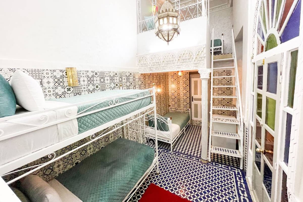 A compact, multi-level room with a patterned floor, a white metal bed, and a staircase.