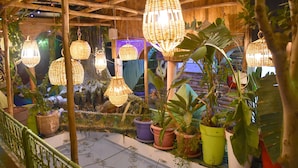 Um espaço ao ar livre coberto com luminárias de vime pendentes, plantas em vasos e piso de azulejos.