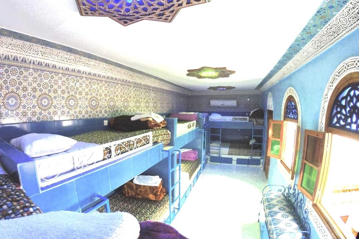 A room with a patterned ceiling, a bed with a patterned bedspread, a bench, and a small table with a box on it.