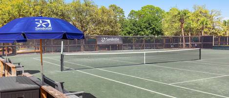 A tennis court with a net, wooden benches, and a blue umbrella.