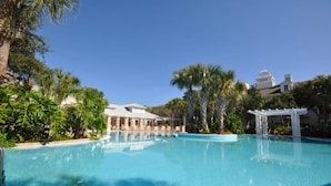 Piscina azul cristalina rodeada por palmeiras e um gazebo branco.
