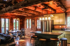 A rustic cabin interior with a wooden dining area, bar stools, and a kitchen with wooden cabinets. - Timber Cove Cabin - a relaxing lakeside retreat (Pittsburg)