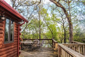 A wooden deck with a table and chairs, overlooking a forested area. - Timber Cove Cabin - a relaxing lakeside retreat (Pittsburg)