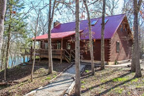 A log cabin with a red roof, surrounded by trees and a gravel path. - Timber Cove Cabin - a relaxing lakeside retreat (Pittsburg)