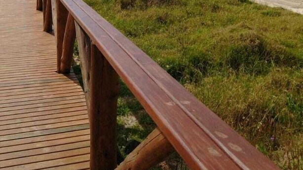 A wooden boardwalk leading to a beach with a person walking in the distance. - Lebanon Praia Hotel (Tramandai)