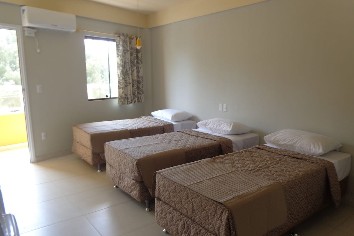 A room with three beds, a window with curtains, and an air conditioning unit.