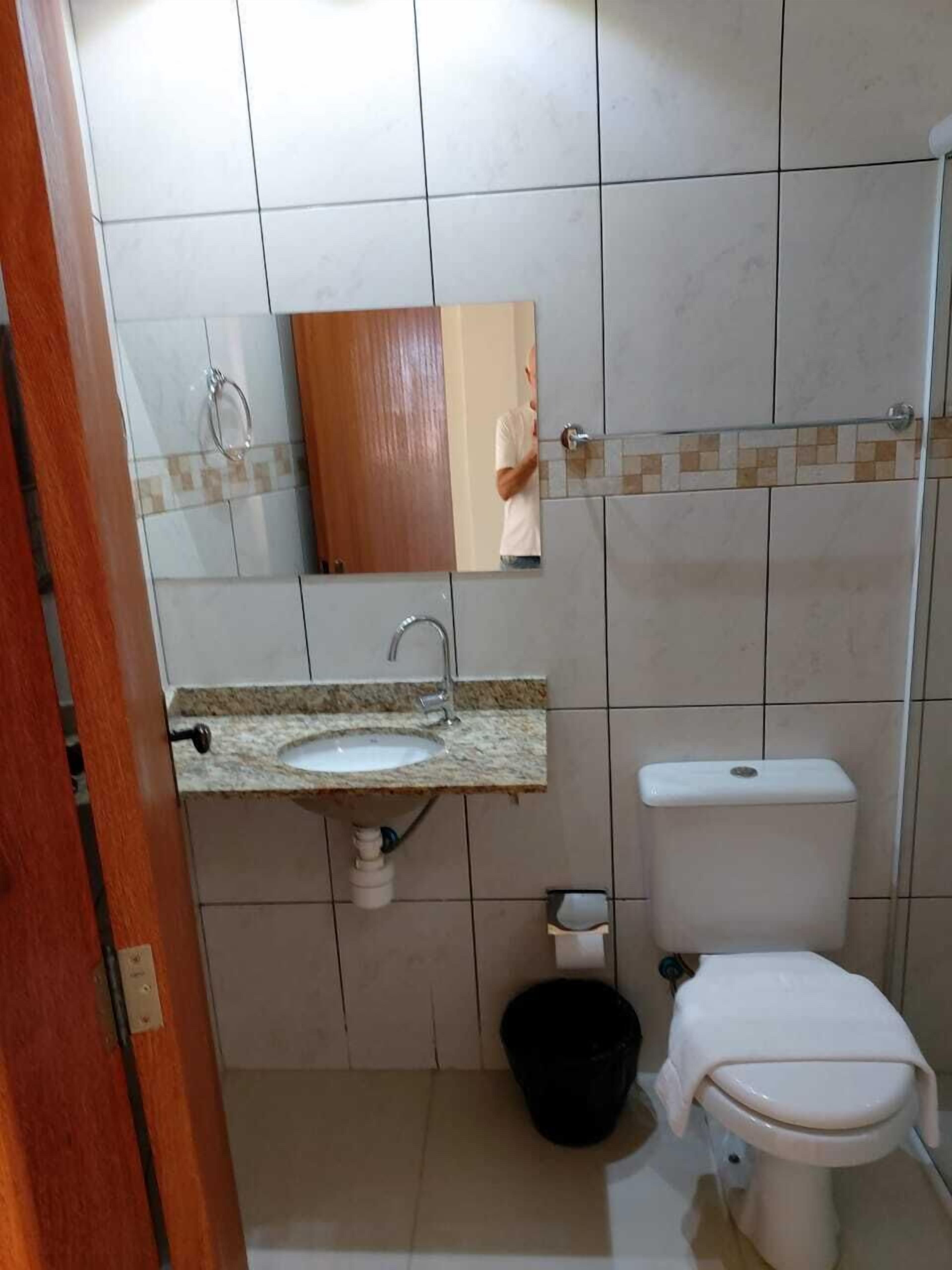 A bathroom with a sink, mirror, toilet, and a black trash bin.