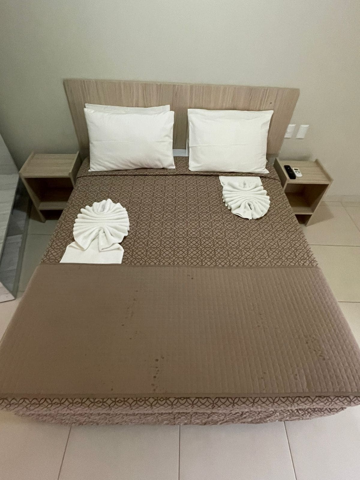 Cama bem arrumada com colcha estampada, dois travesseiros e toalhas dobradas decorativas.
