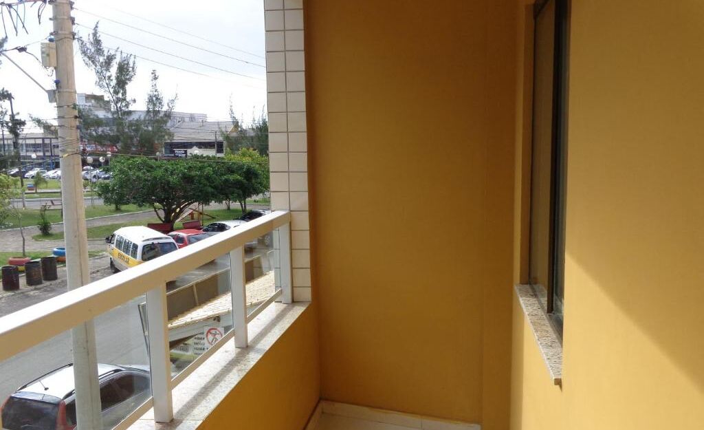 A balcony with a yellow wall, a view of a parking lot, and a tree.