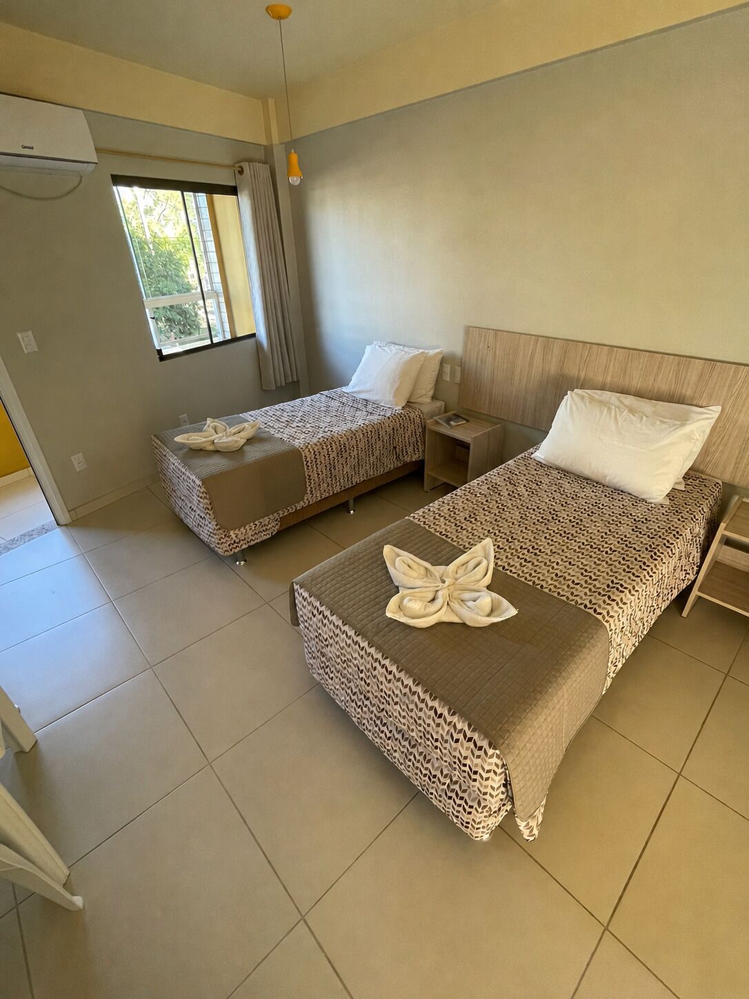 Una habitación de hotel con dos camas, una ventana, un ventilador de techo y una puerta.