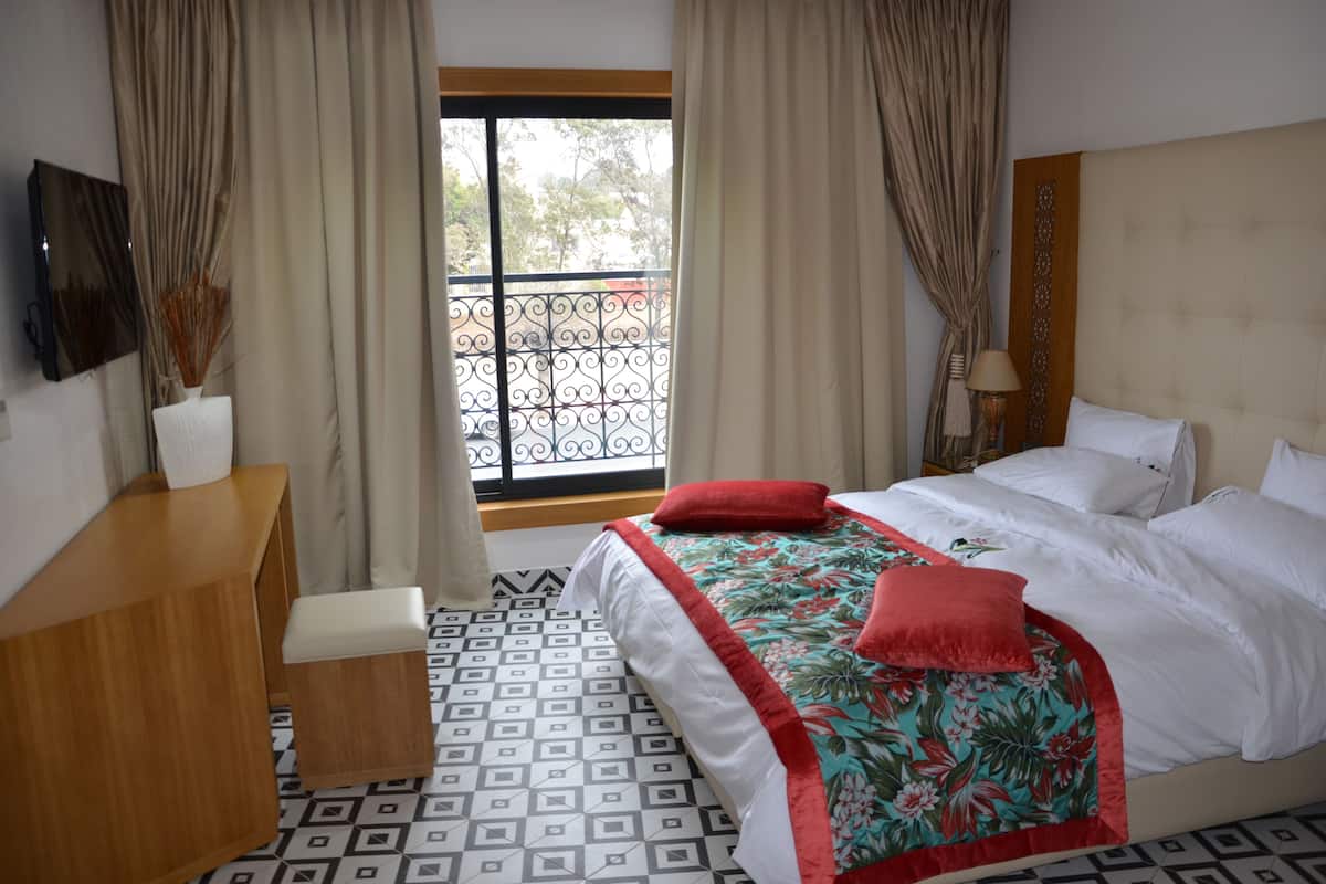 Ein Hotelzimmer mit Bett, Schreibtisch, einem Fenster mit Vorhängen und einem gemusterten Boden.