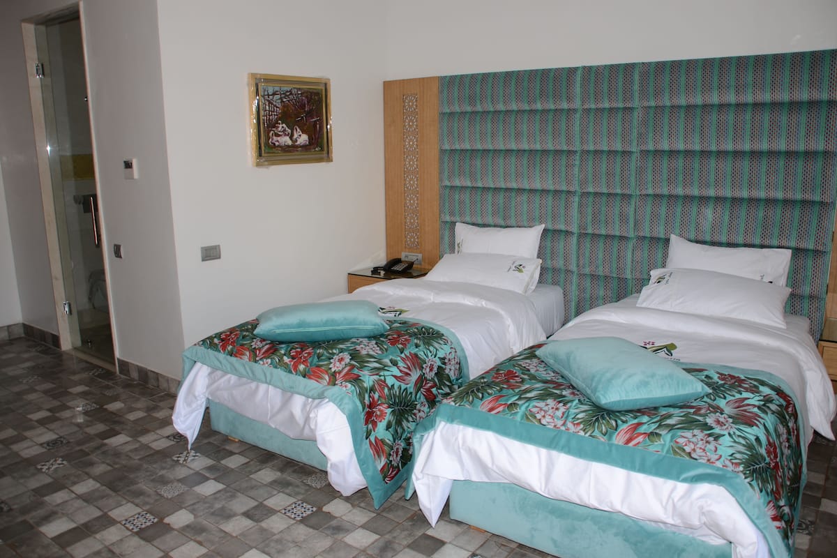 Ein Hotelzimmer mit zwei Betten, einem Holz-Kopfteil, einem kleinen Nachttisch und einem gerahmten Bild an der Wand.