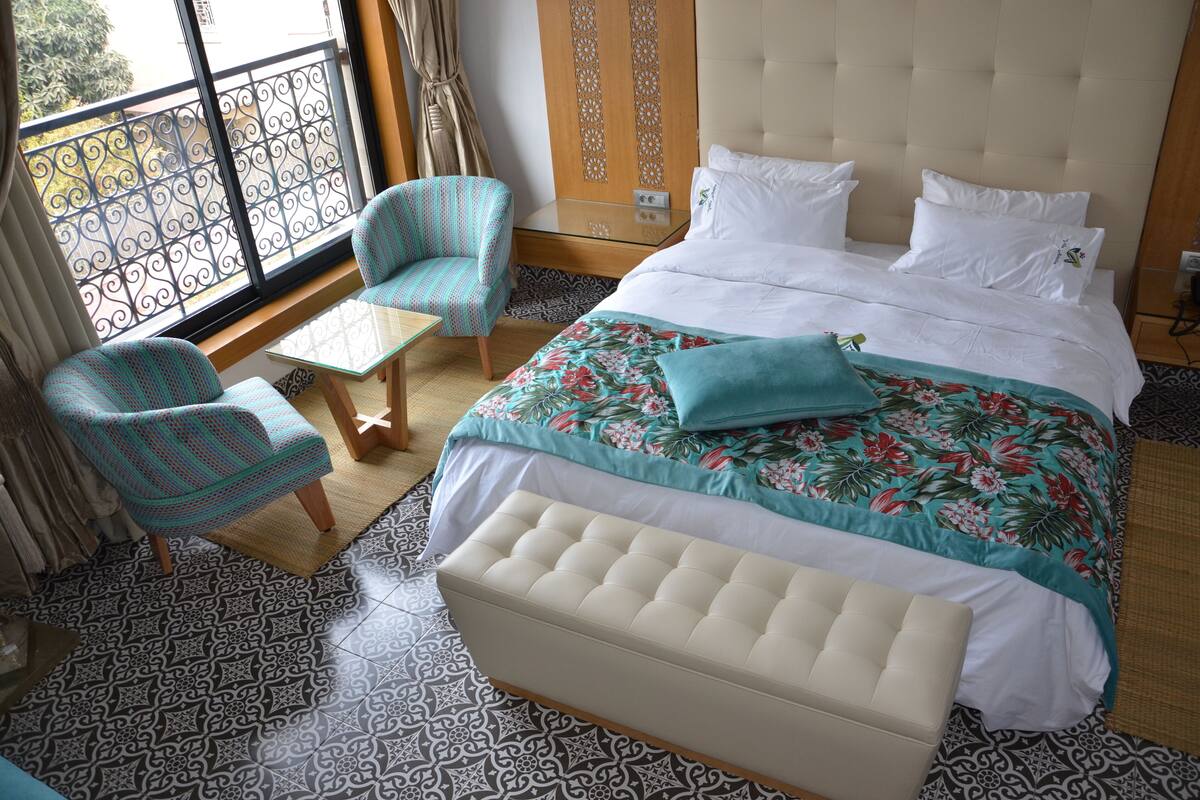 Ein Hotelzimmer mit einem Bett, einer Bank, zwei Stühlen, einem kleinen Tisch und einem gemusterten Boden.