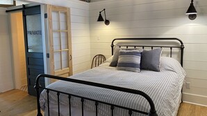 Un dormitorio con estructura de cama metálica, una puerta de madera con la leyenda “PRIVATE” y techo inclinado con ladrillo a la vista.