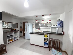 A compact kitchen with white appliances, a central island, and a bar stool. - 111, Ground Floor Apartment (Bombas)