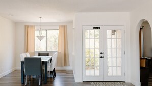 Un coin repas avec une table et des chaises, une porte blanche avec une pancarte, et une vue par la fenêtre.
