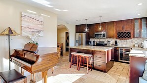 A spacious kitchen with a piano, wooden cabinets, granite countertops, and a large island.