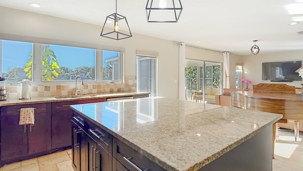 A modern kitchen with a large island, dark cabinetry, and pendant lighting.