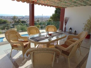 Un balcón con mobiliario de mimbre, una mesa de vidrio y vistas a la ciudad.