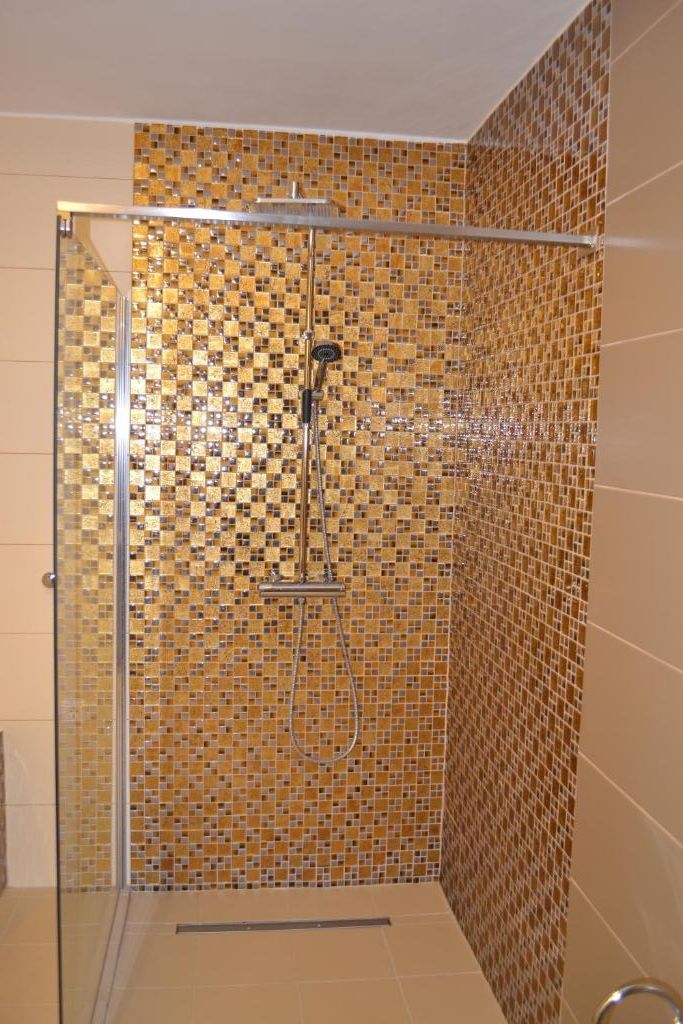 A shower with a glass door and mosaic tile walls.