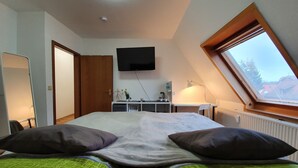 Une chambre à coucher avec un lit, deux oreillers, un bureau avec un ordinateur, une télévision et une lucarne.