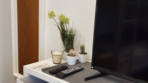 Un meuble pour télévision avec une télécommande, une bougie en verre et deux plantes en pot.