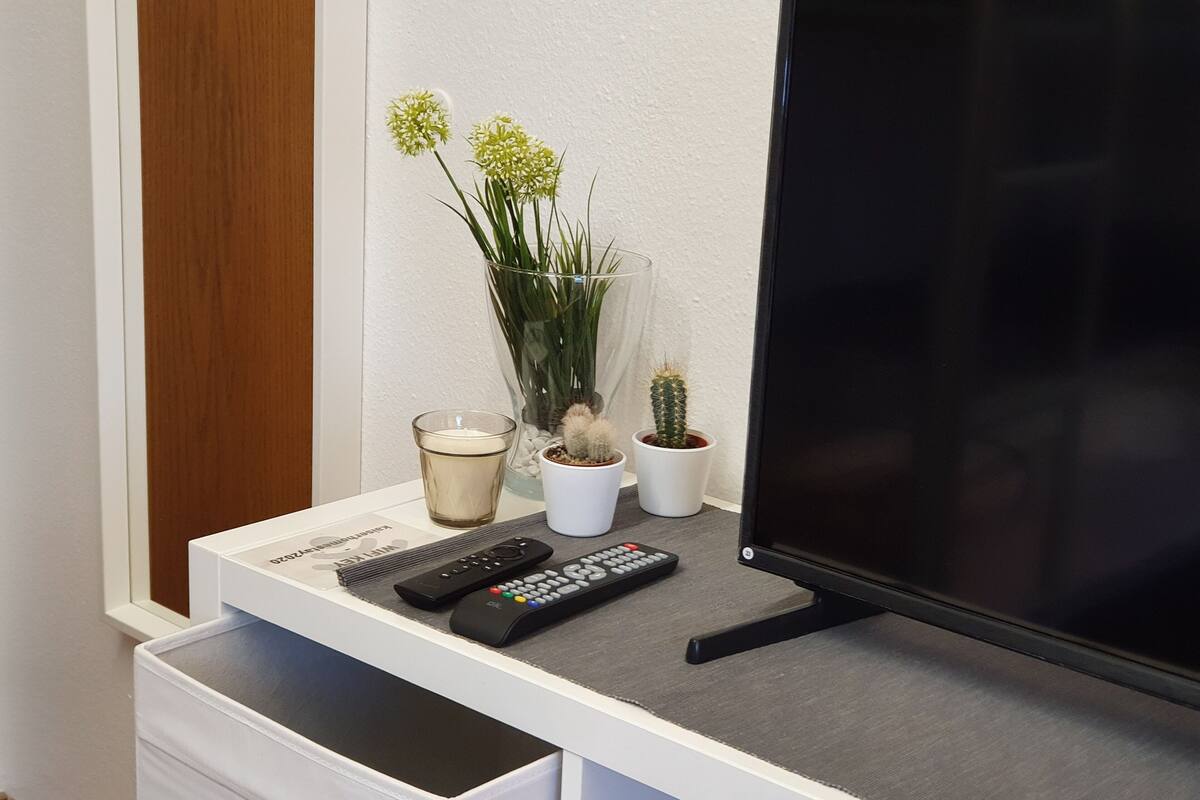 A TV stand with a remote control, a glass candle, and two potted plants.