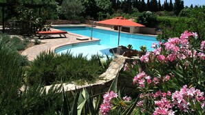 A swimming pool with a red umbrella, surrounded by greenery and a stone wall. - Casa Rustico, large pool, 350m from the beach, by the river. (Chia)