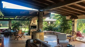 An outdoor patio area with a stone fireplace, seating arrangements, and a view of the garden. - Casa Rustico, large pool, 350m from the beach, by the river. (Chia)