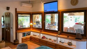 A cozy room with a large window, a wooden bench, and a TV mounted on the wall. - Casa Rustico, large pool, 350m from the beach, by the river. (Chia)