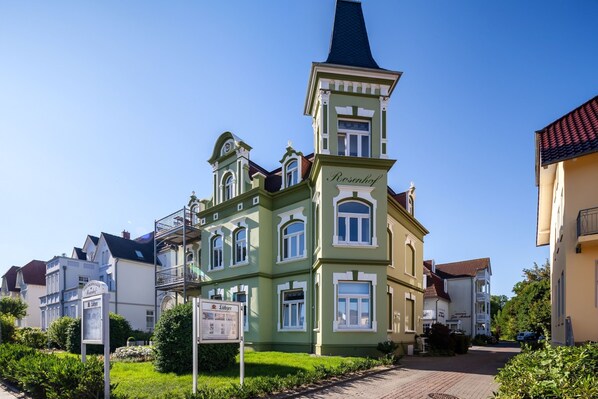 A historic building with a prominent tower, a signboard, and a well-maintained garden.